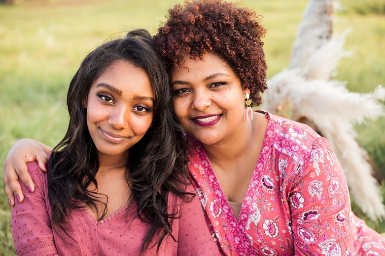 A mom and teen daughter dressed in boho style pose in front of boho decorations and a field and pond in the country in Oklahoma