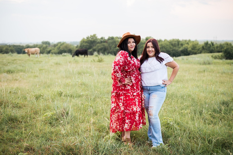 A mom and teen daughter dressed in boho style pose in front of cattle grazing in a field in the country in Oklahoma