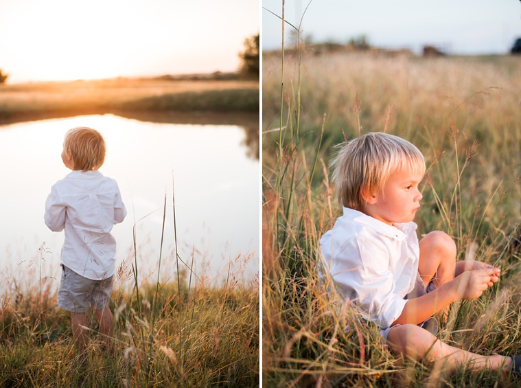 A young boy looks out at a pond with the sunset behind it; the young boy sits in the grass in a field at a family photo session in Tuttle, Oklahoma