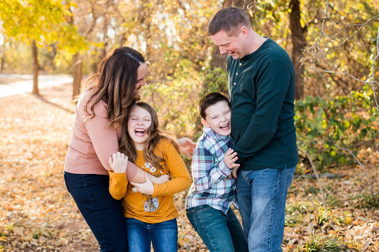 a mom and dad tickle and laugh with their son and daughter at a family photo session in Oklahoma at a park in the fall