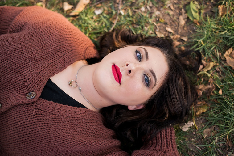 Professional photo of a senior girl laying in the grass on her back and looking up at the camera with a serious expression at Will Rogers Gardens in Oklahoma City, Oklahoma