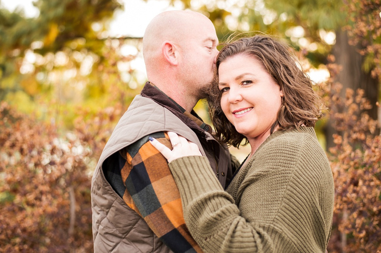 A husband and wife hug with the husband kissing her temple with fall color all around them at Will Rogers Gardens in Oklahoma City, Oklahoma