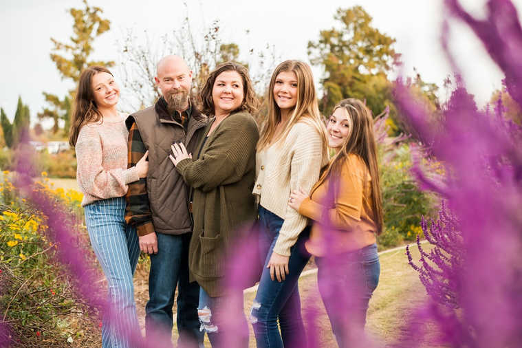 A mom and dad with 3 teen daughters stand and smile together in a flower garden with purple flowers in foreground  in the fall at Will Rogers Gardens in Oklahoma City, Oklahoma