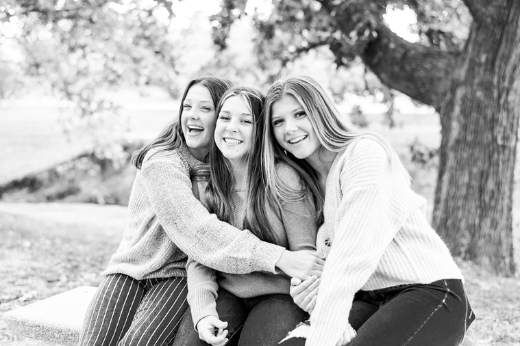 Black and white photo 3 teen sisters sit and laugh together on a bench with trees around them at Will Rogers Gardens in Oklahoma City, Oklahoma