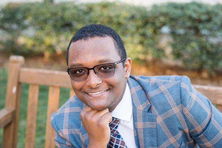 close up portrait of an african-american high school senior boy wearing a patterned suit and smiling as he sits on a bench on the OU campus in Norman Oklahoma