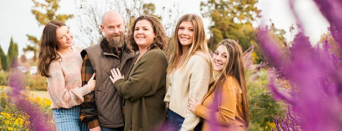 a mom and dad stand with their 3 teen daughters and smile and hug together with yellow flowers around them and with purple foreground flowers framing them at Will Rogers Gardens in Oklahoma City