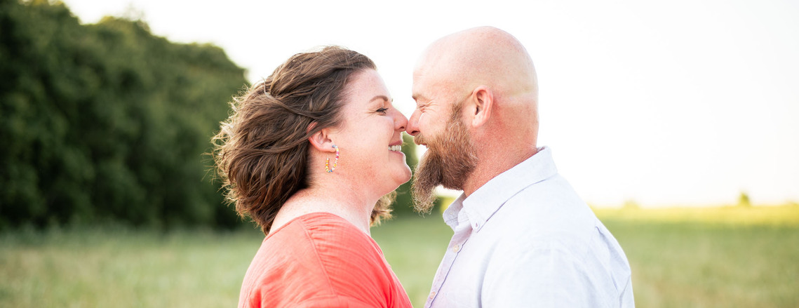 A husband and wife pose in front of a grassy meadow at sunset in Oklahoma