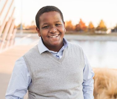 young teen boy smiles standing by Devon boathouse with the oklahoma river in the background for family photos