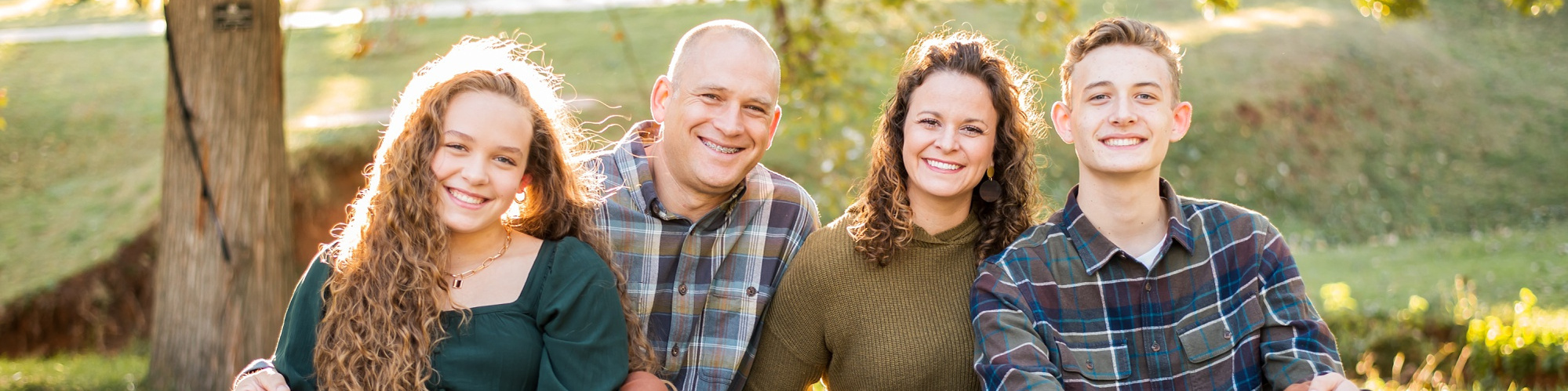 a family of 4 with teen kids sit together and smile at Will Rogers Park in Oklahoma City, Oklahoma at a fall photo mini session by Cheryl Jackson Photography