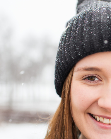 close up portrait of half a face of a high school senior girl wearing a black beanie smiling while she stands in the snow in a park in Tuttle Oklahoma