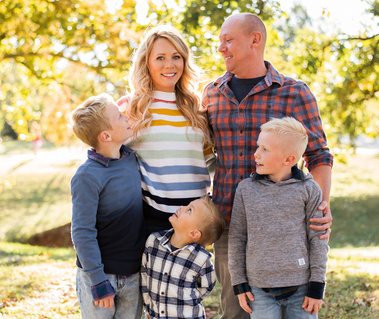 a family of 5 stand together and everyone is looking and smiling at the mom at Will Rogers Park in Oklahoma City, Oklahoma at a fall photo mini session by Cheryl Jackson Photography