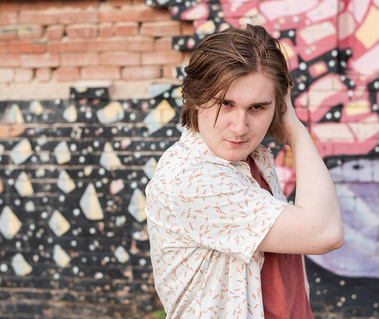 senior boy in a button down shirt making a funny dramatic face in front of a colorful wall mural in midtown Oklahoma City