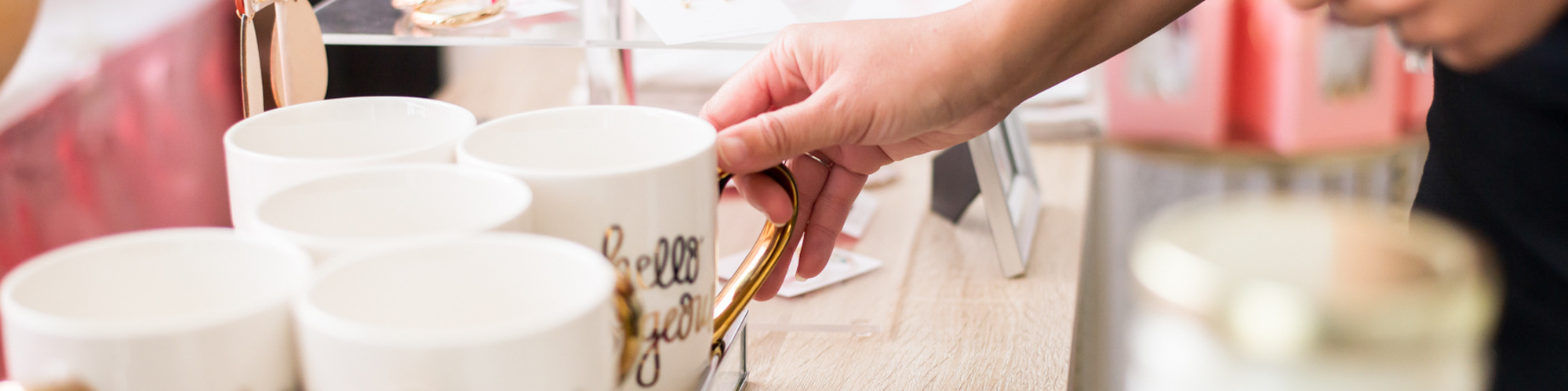 close up of a boutique shop owner placing a white mug with gold handle out for display on a table  with other merchandise around it at a branding session in Oklahoma City