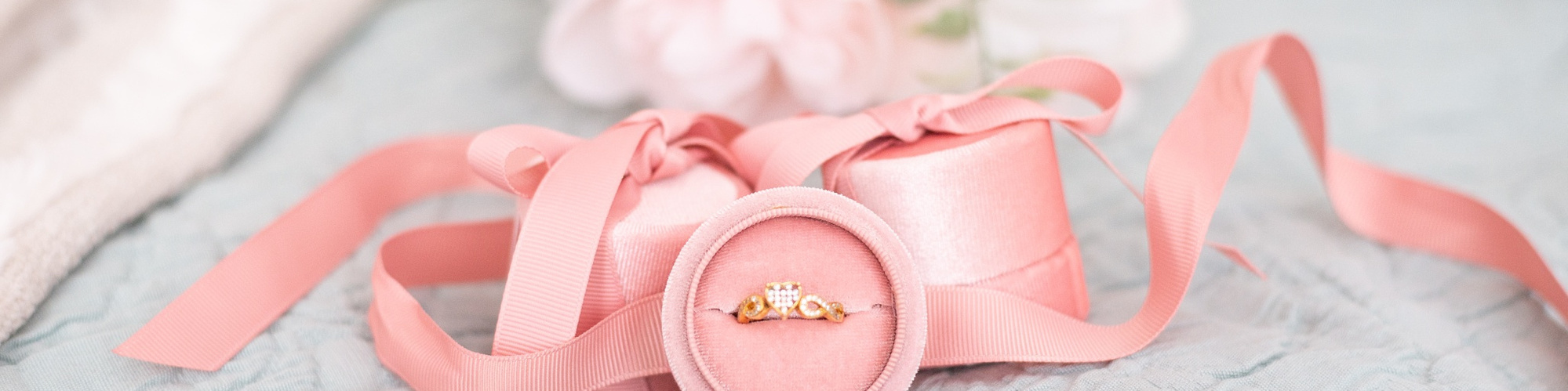 close-up product image of a simple gold ring in a pretty pink box with pink ribbon and white flowers around it at a product brand shoot in Oklahoma city