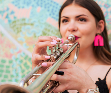 pretty senior girl plays a trumpet wearing a black dress and pink earrings standing in front of a colorful wall mural, taken by Oklahoma City senior photographer