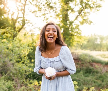 High school senior girl holds a flower and laughs in her senior photos in Oklahoma