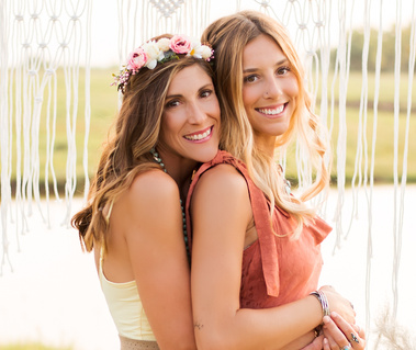 A mom and teen daughter hug together dressed in boho accessories in front of a macrame curtain at a photo shoot near Oklahoma City, Oklahoma.