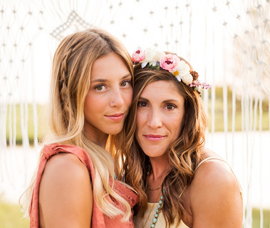 an adult daughter and her mom dressed in boho style stand close together and soft smile at the camera in a field in central Oklahoma