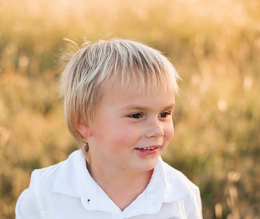 a young boy with blond hair smiles off camera with golden prairie grass behind him in a field in central Oklahoma