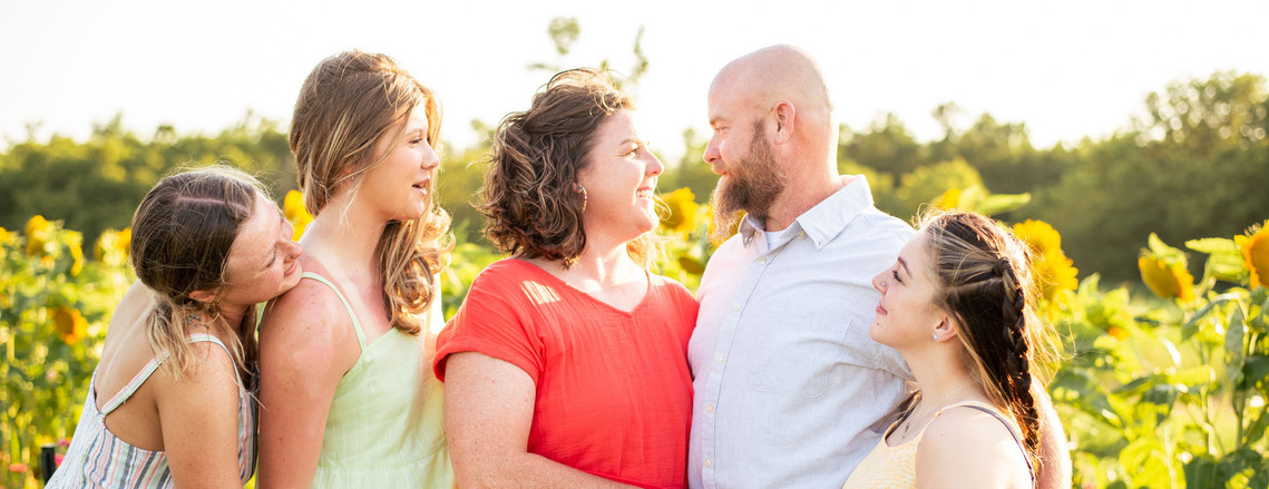 Parents and their three teenage daughters pose in front of a flower meadow at sunset in Oklahoma