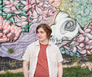 senior boy in a button down shirt making a funny dramatic face in front of a colorful wall mural in midtown Oklahoma City