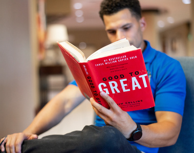 a valet company business owner wearing a blue shirt with dark curly hair sits and reads a self-improvement book inside a hotel lobby in downtown Oklahoma City