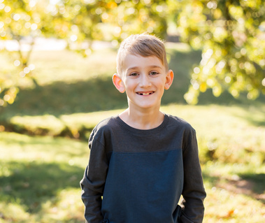 A young boy stands and smiles at Will Rogers Park in Oklahoma City, Oklahoma at a fall photo mini session by Cheryl Jackson Photography