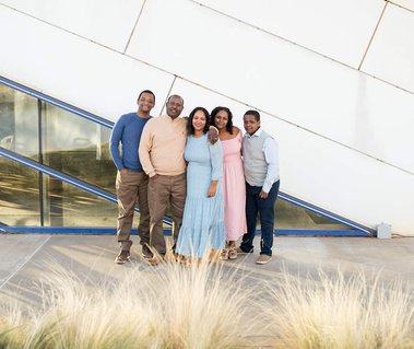 mom, dad and three teen children stand and hug and smile in front of the Devon Boathouse in Oklahoma City for family pictures