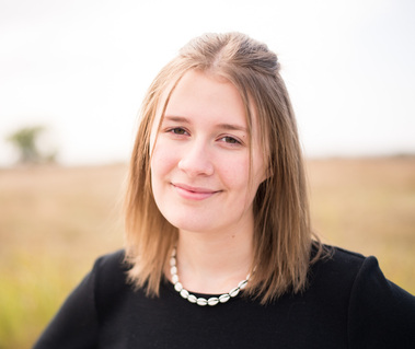 Close up portrait of a teenage girl in a black t-shirt in front of a field with a soft smile