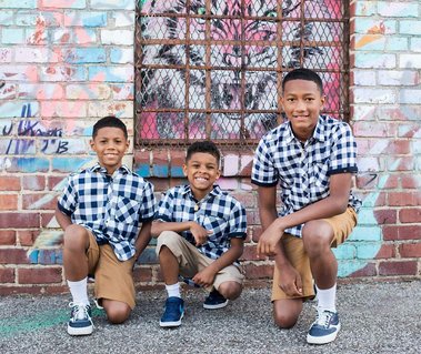 three young brother kneel together and smile in front of a tiger mural on a brick building in Oklahoma City
