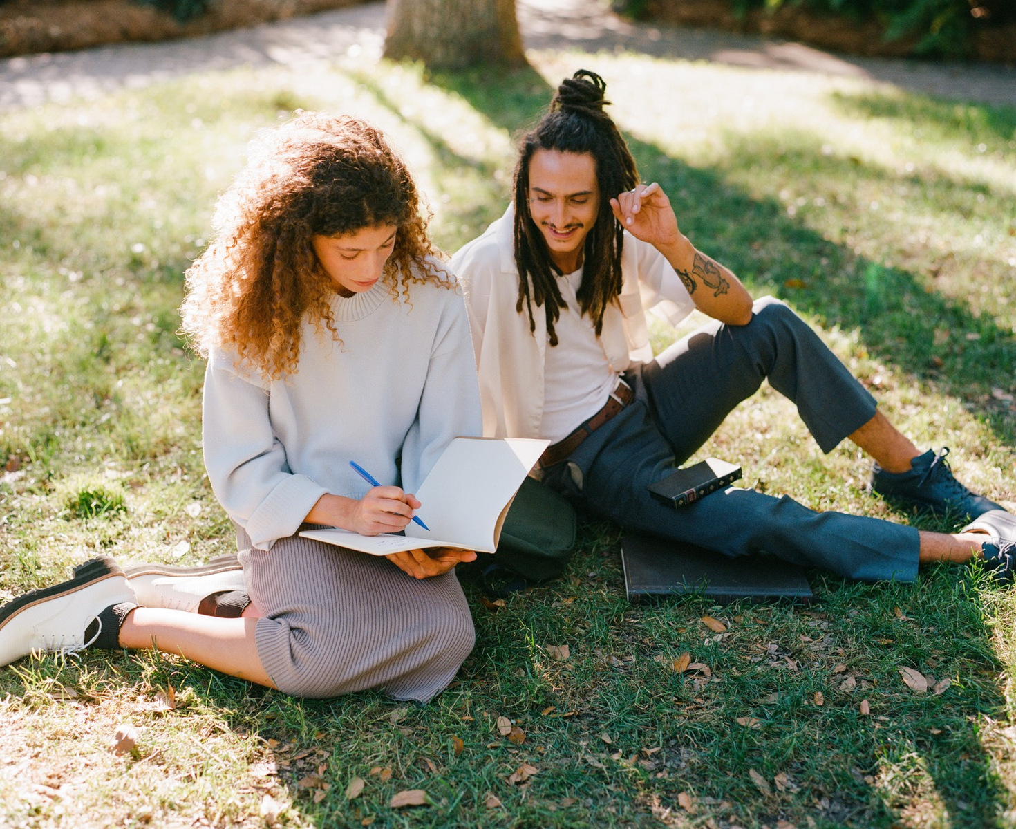 Two students sit together in a grassy lawn with BookBook products
