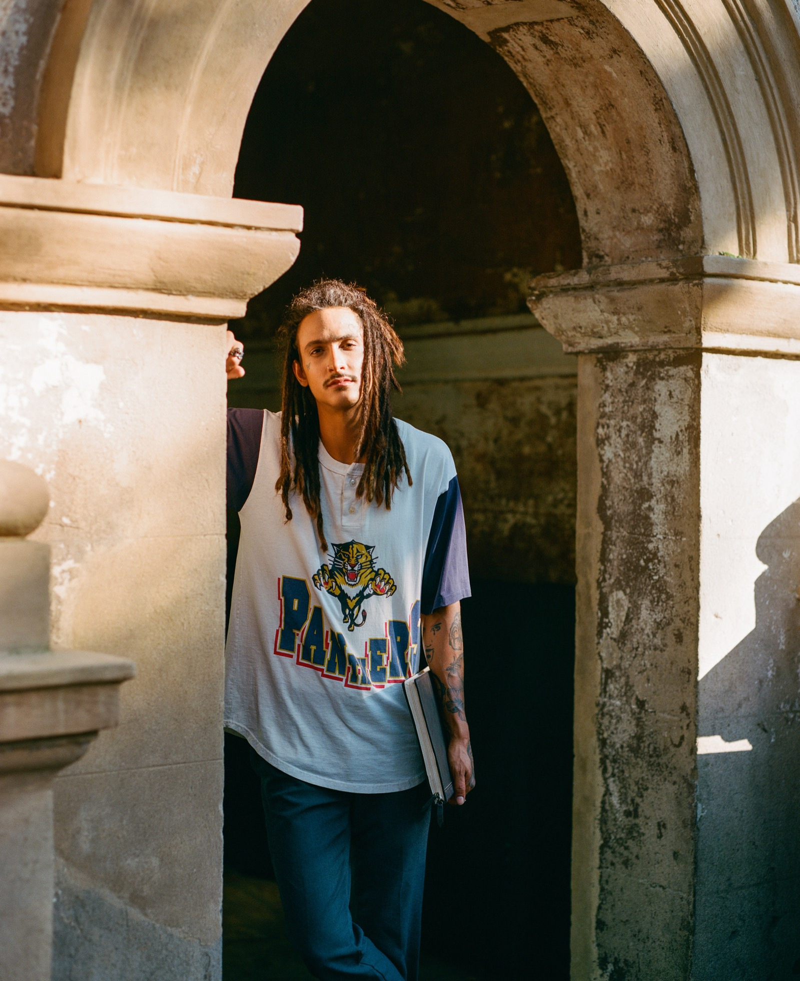 A stoic student leaning against a textured archway on a historic college campus