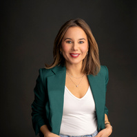 Professional and casual business woman in green blazer and jeans smiling into camera on black background. 