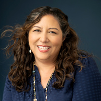 Woman on blue background in blue shirt smiling at camera. Clothing styling by Image Concepts.