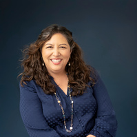 Woman on blue background in blue shirt smiling at camera. Clothing styling by Image Concepts.