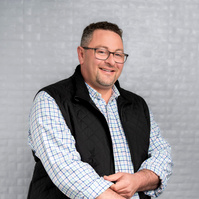 Man with glasses standing in vest jacket. Clothing styling by Image Concepts.