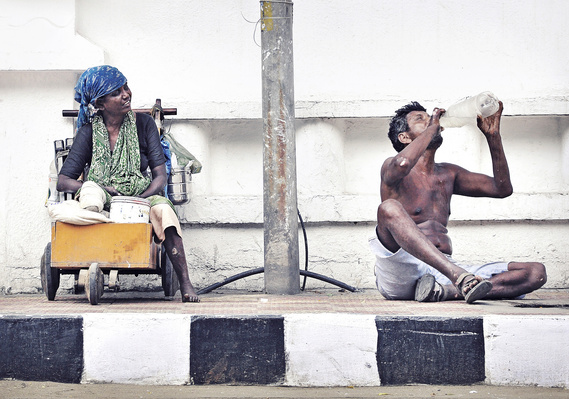 Disabled woman on a push cart and man on the pavement drinking water from a water bottle