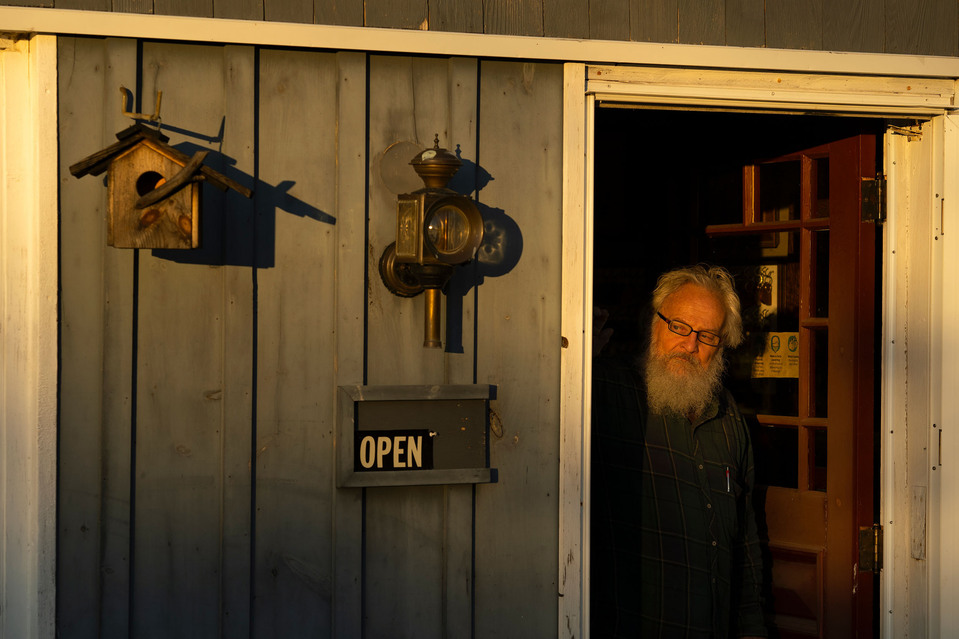 A man with a beard peeks out from a doorway as the sun sets.