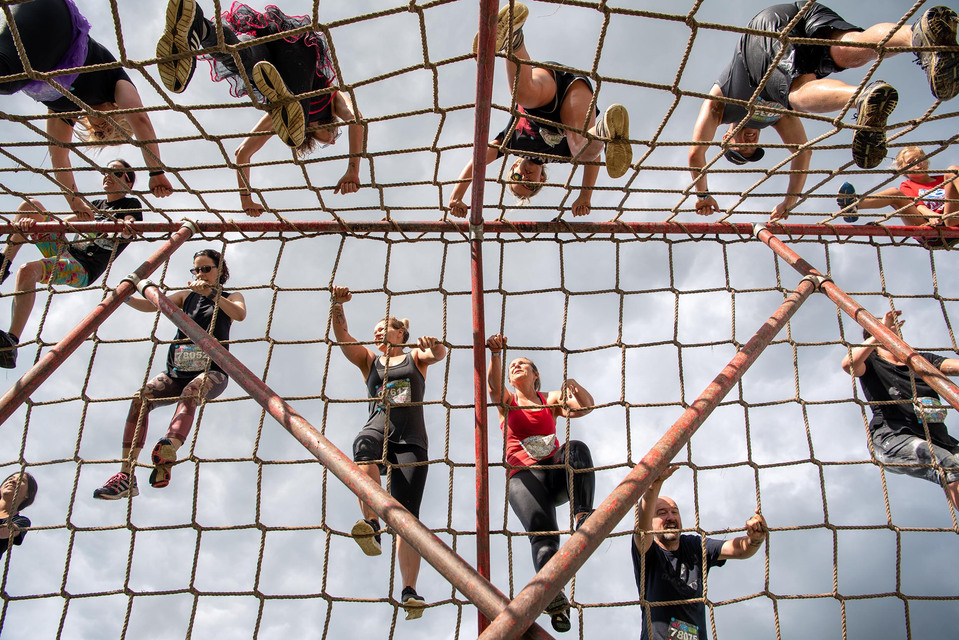 People are photographed from below while climbing a rope ladder obstacles during an obstacle course race.