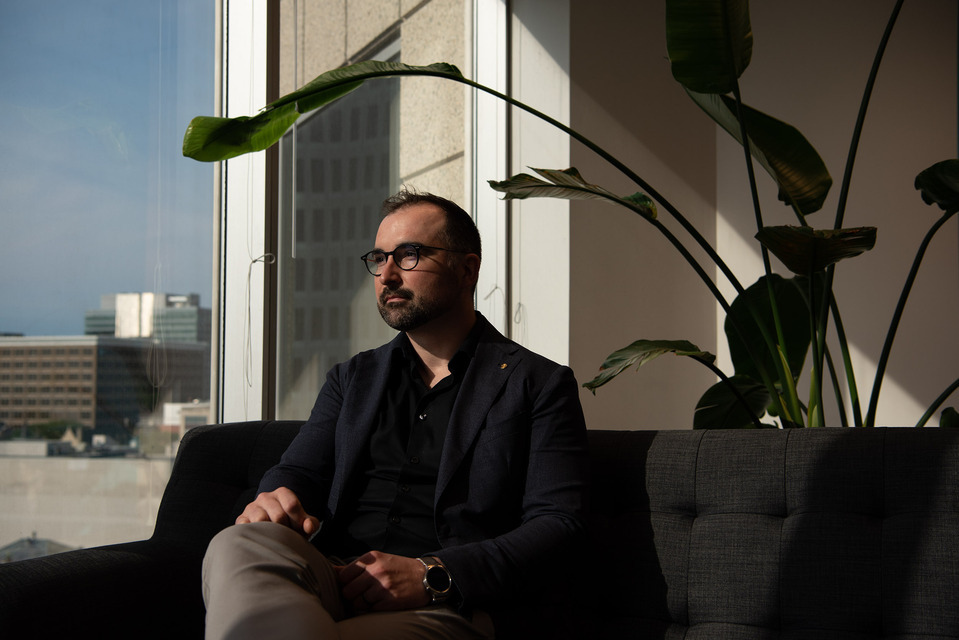 A man poses for a portrait in an office building with a large plant in the background.