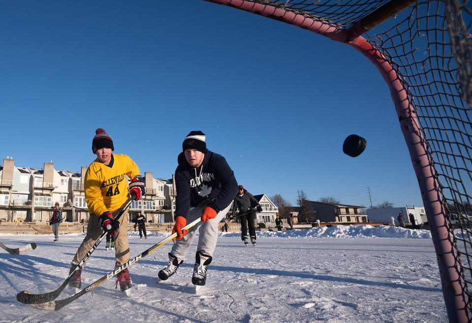 A hockey puck is frozen in the air during an outdoor ice hockey game.