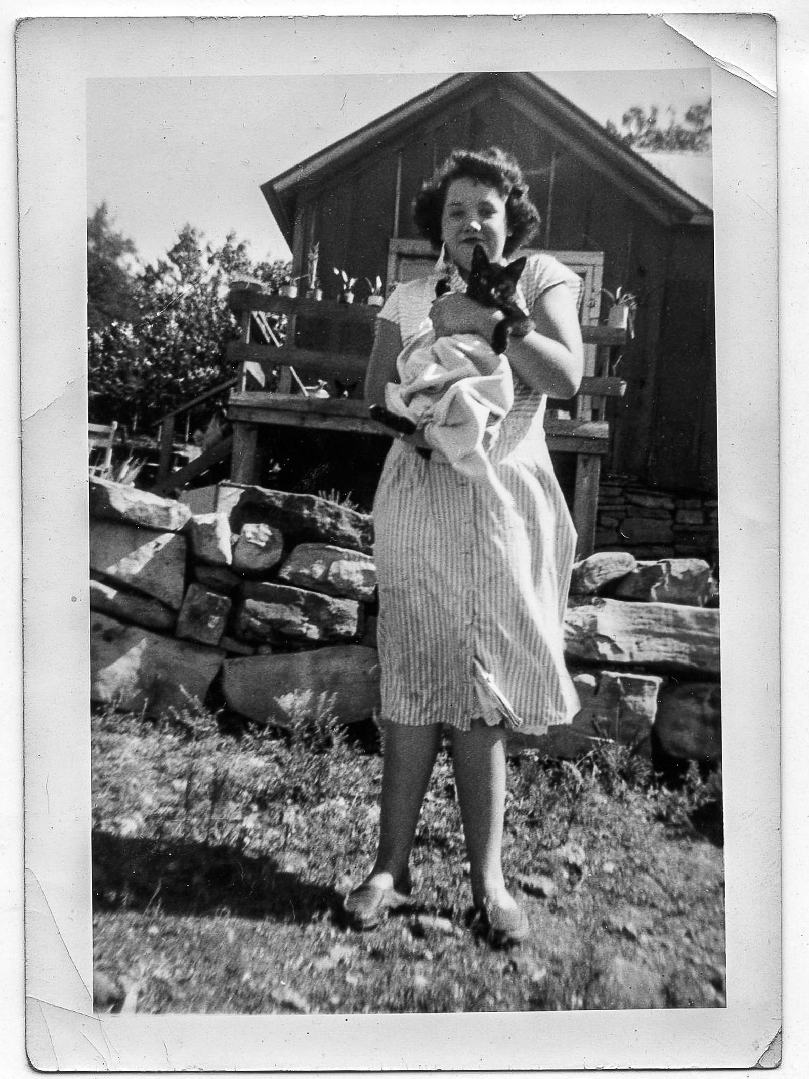 Vintage Black & white photo of young woman in front of shack, holding a black cat.