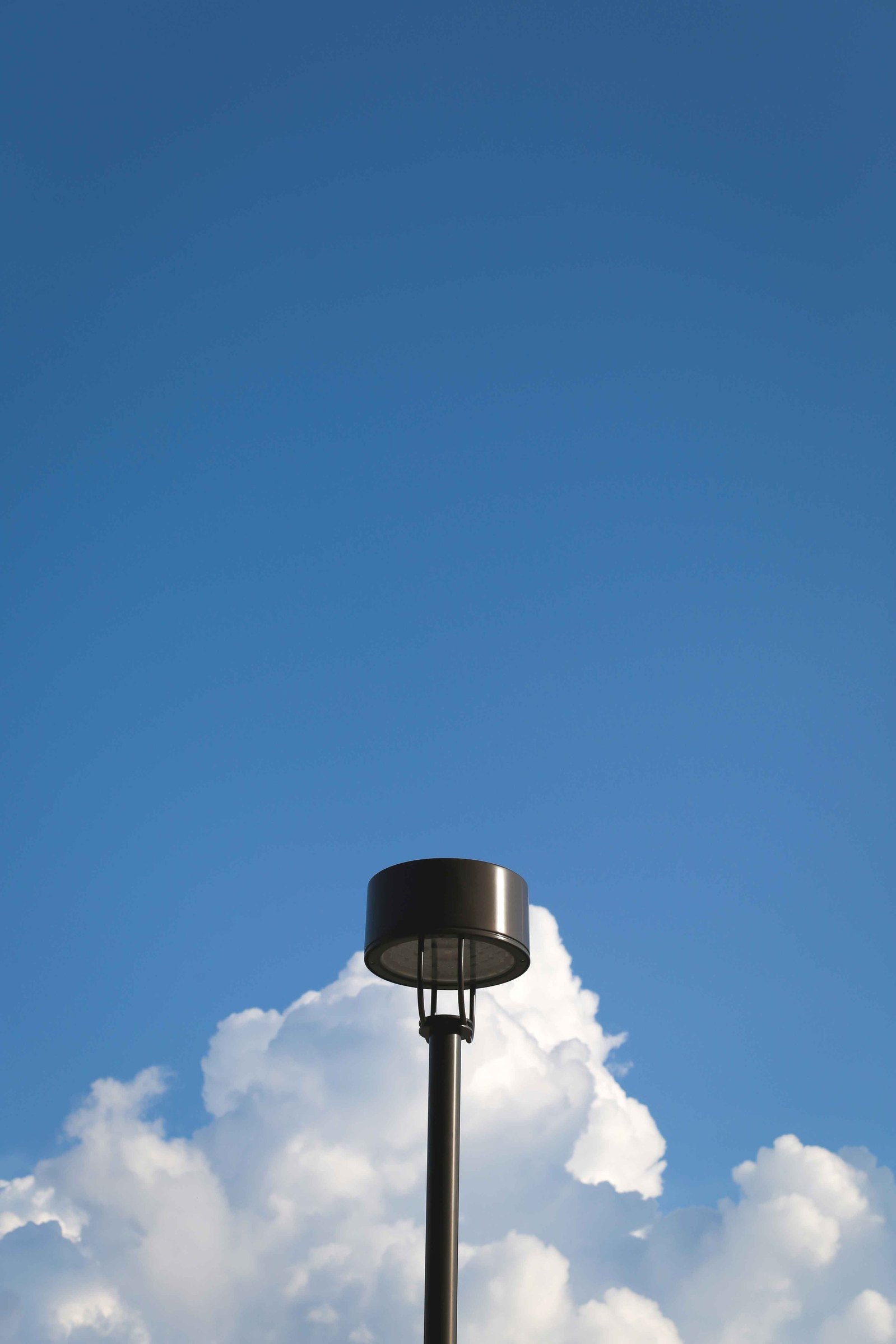 An image of a single lamp post against the blue sky and fluffy white clouds.