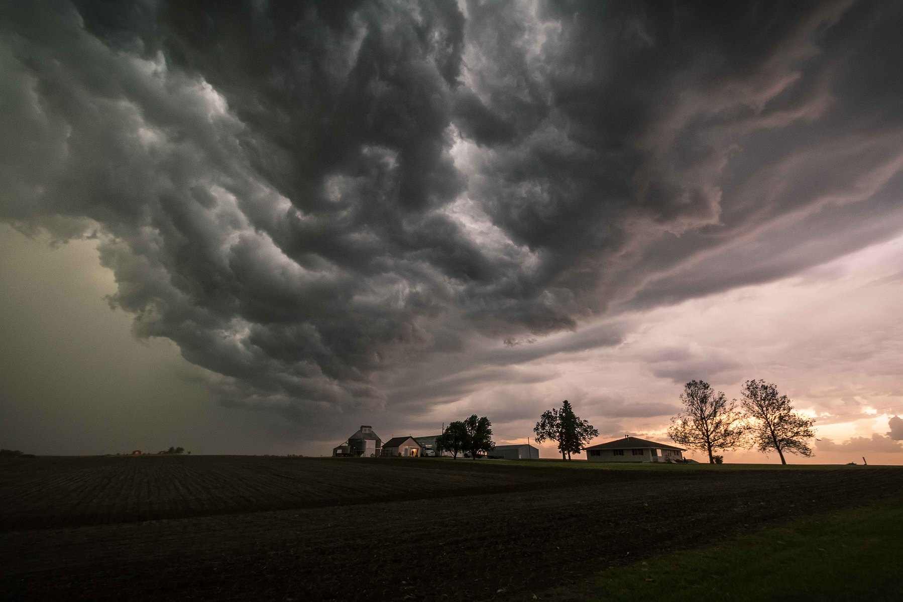 Violent dark storm clouds swirl over a tiny farm house in rural Nebraska.