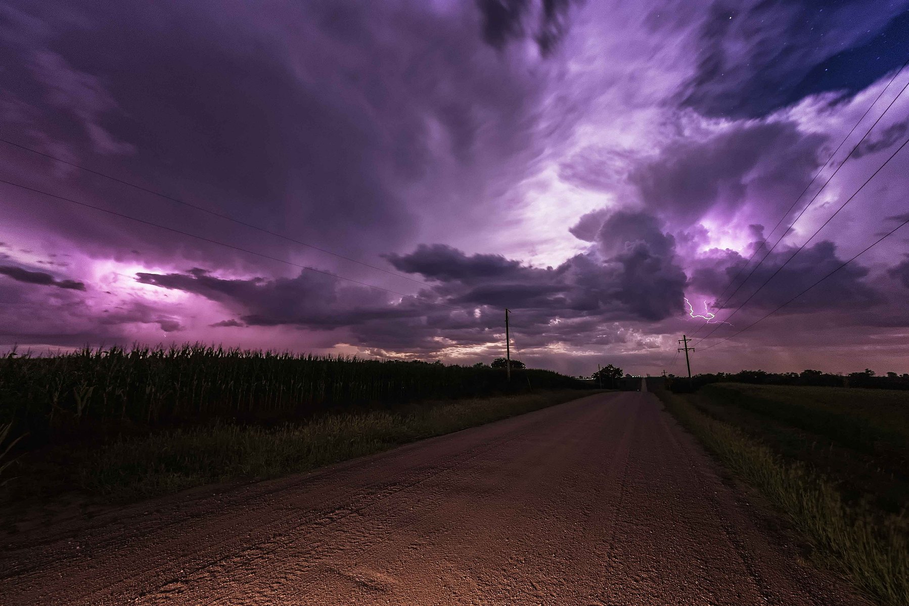 Looking at a purple colored storm at the end of a long dirt road at night in Nebraska