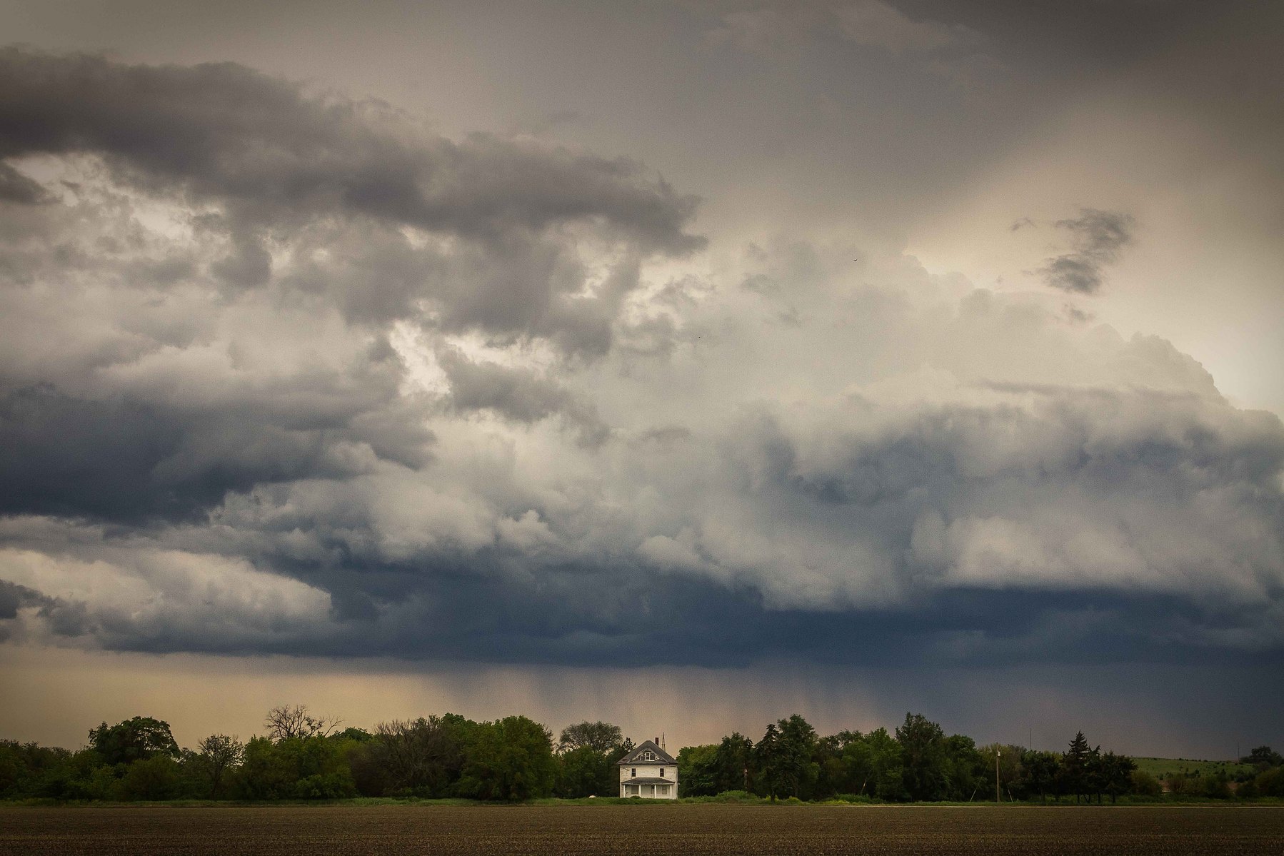 A tiny house is in the middle of the frame with ominous storm clouds hanging above in Nebraska.
