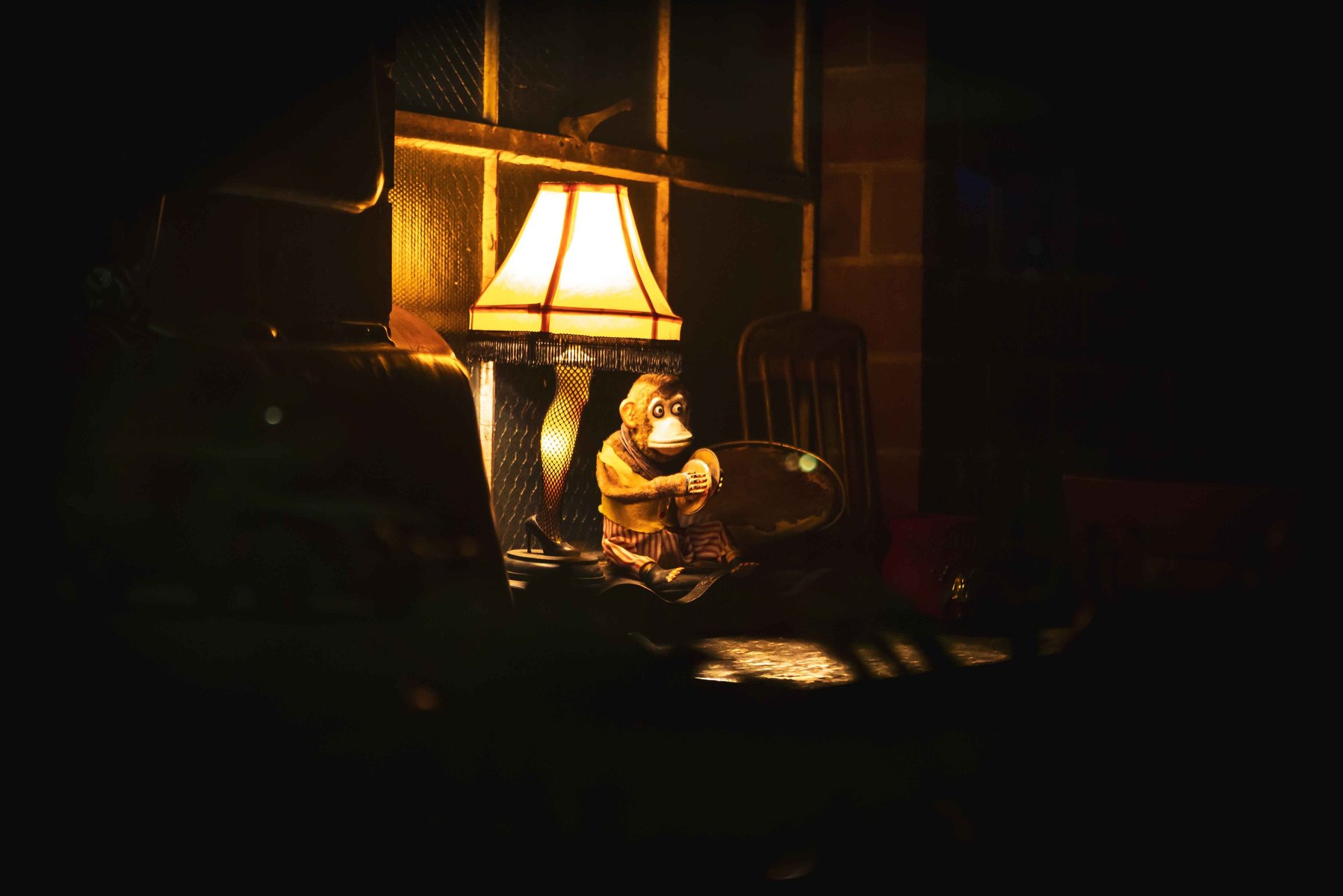 A toy monkey with cymbols under a lamp in a dark room.