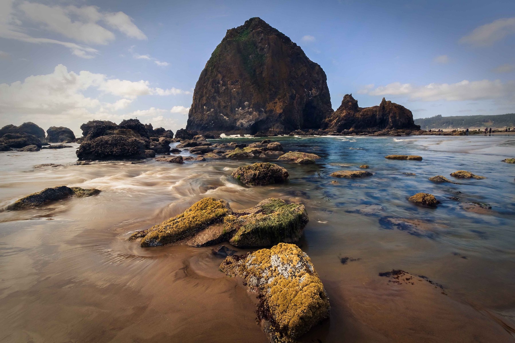 Beautiful textured rocks leading up to a massive stone edifice in the distance at Cannon Beach in Portland Oregon.