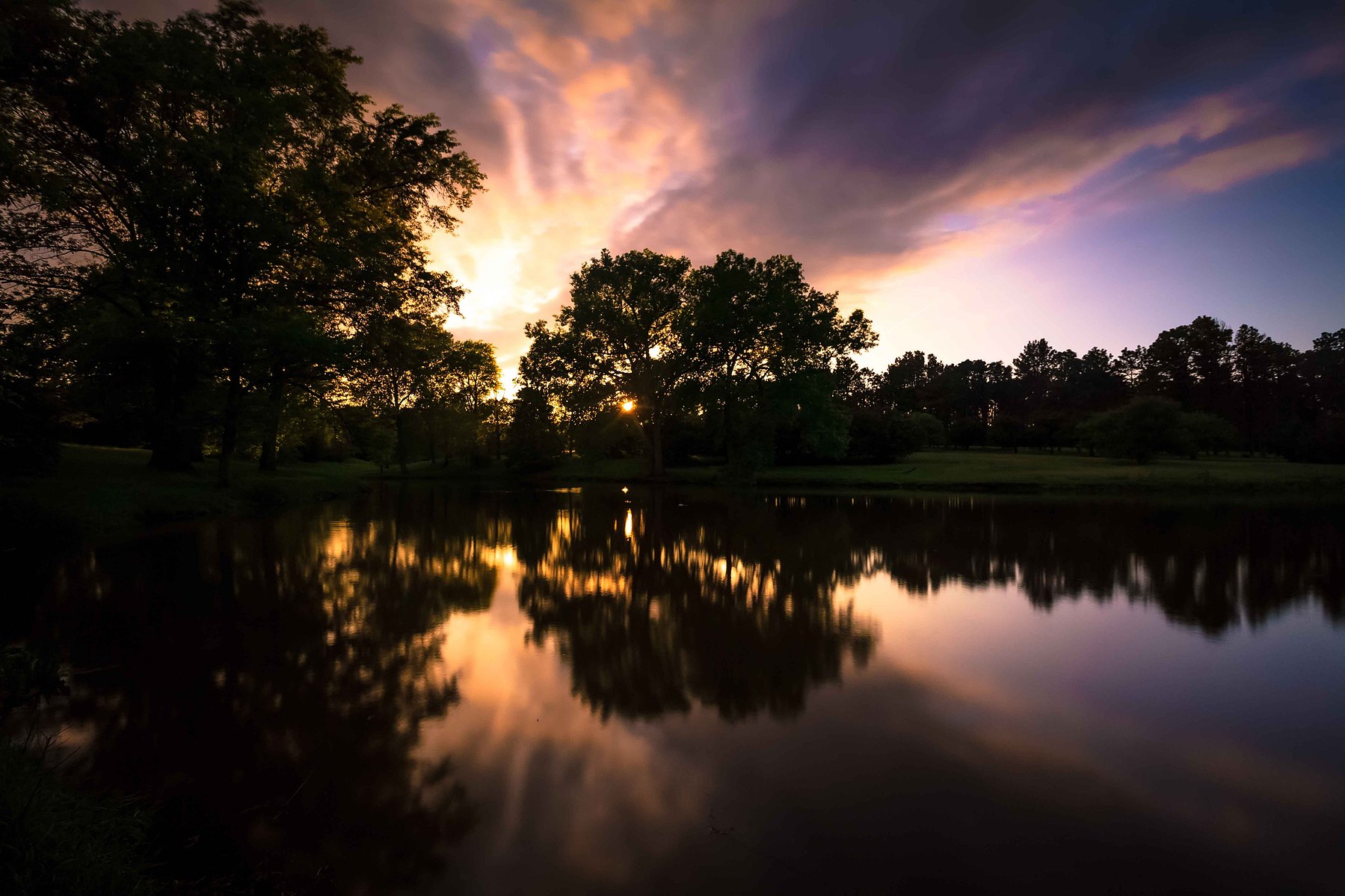 A dramatic sunset sky filled with purples, pinks and oranges over a still lake against a silhouetted backdrop in Nebraska.