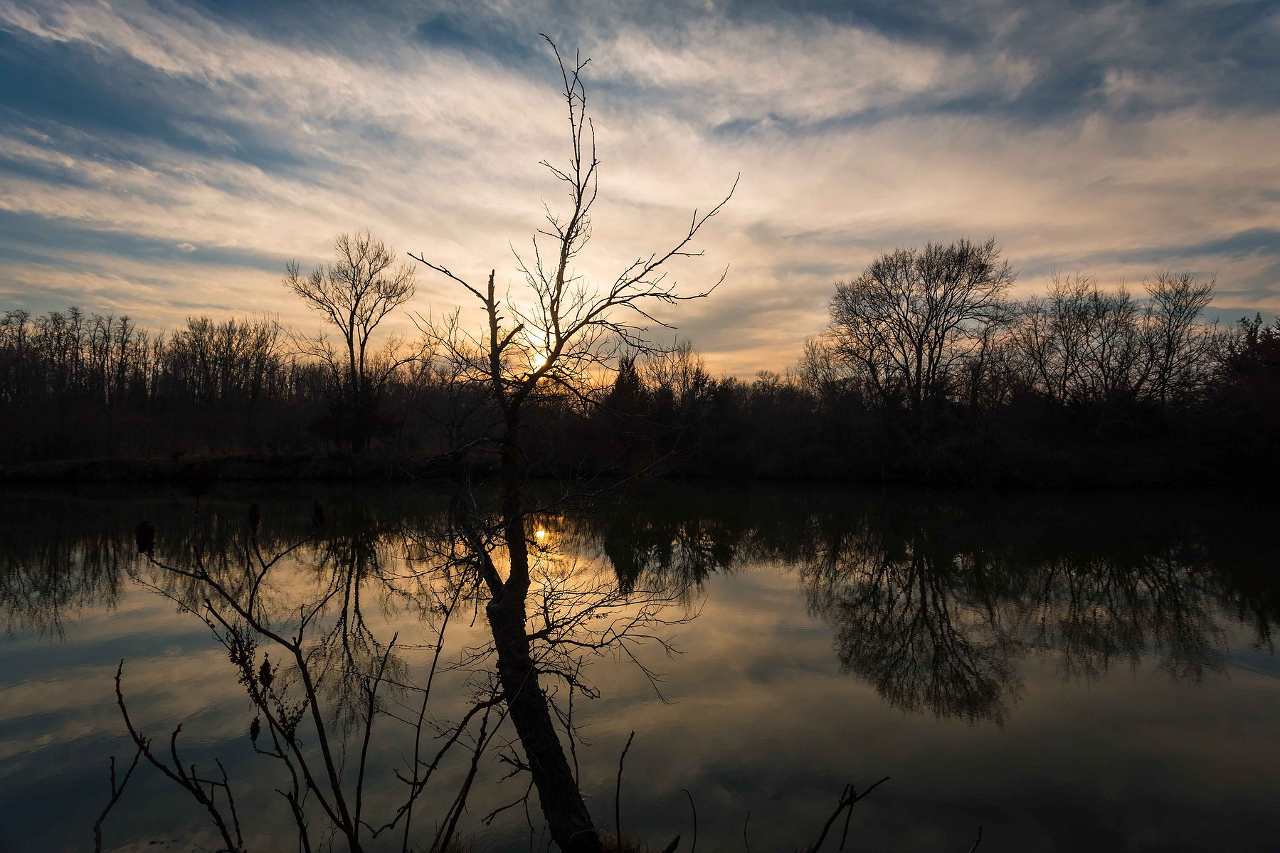 A beautiful sunset draped across the sky against a silhouette background and perfectly still water reflecting the shadows and sky.